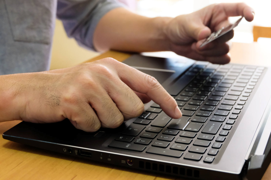 Male hand holding credit card, entering payment information on keyboard for order online shopping