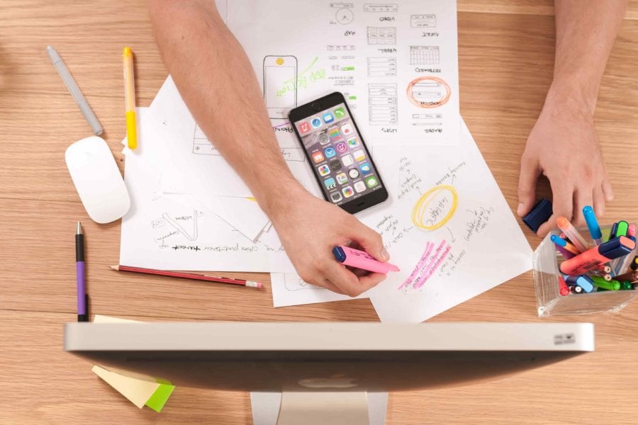 Flat-lay image of hands drawing and creating plans in front of computer and mobile phone