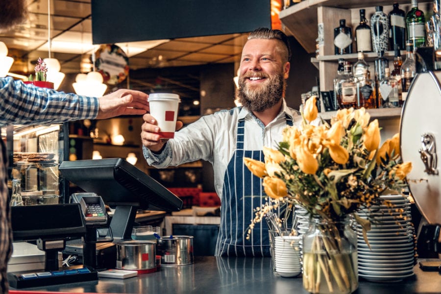 Happy barista male selling coffee to a consumer in a coffee shop