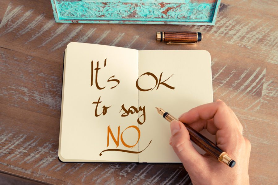 Woman hand writing a note with a fountain pen on a notebook. Handwritten text IT'S OK TO SAY NO, business success concept.