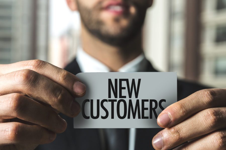 New Customers sign being held up by a businessman blurred out in the background