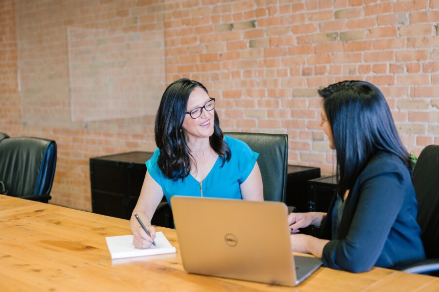 Two women sat discussing work at a desk with a laptop