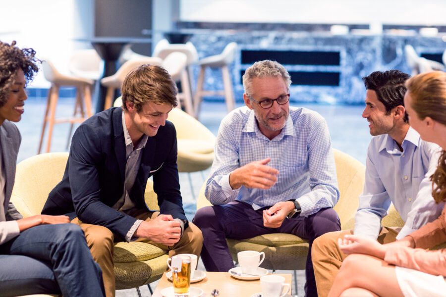 A group of people sitting in chairs in a cafeteria, talking and drinking coffee