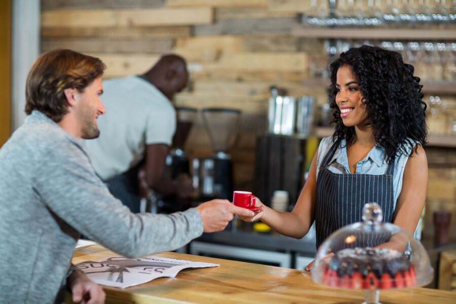 Smiling waitress serving a cup of coffee at a counter in a café.