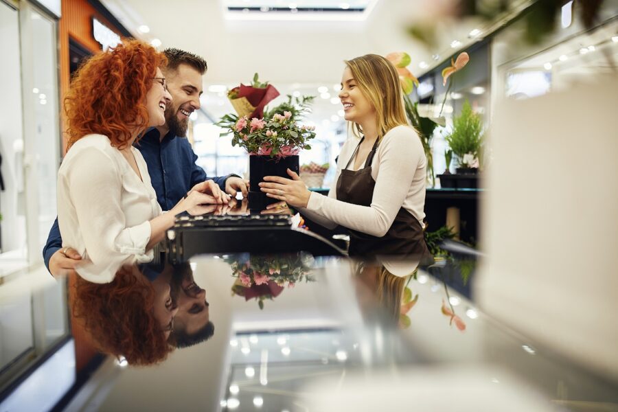 Happy couple and shop assistant with potted plant at counter in flower shop